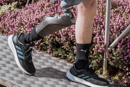 Beinprothese Bein mit Prothese in einem sportlichen Schuh, umgeben von blühenden Pflanzen.
